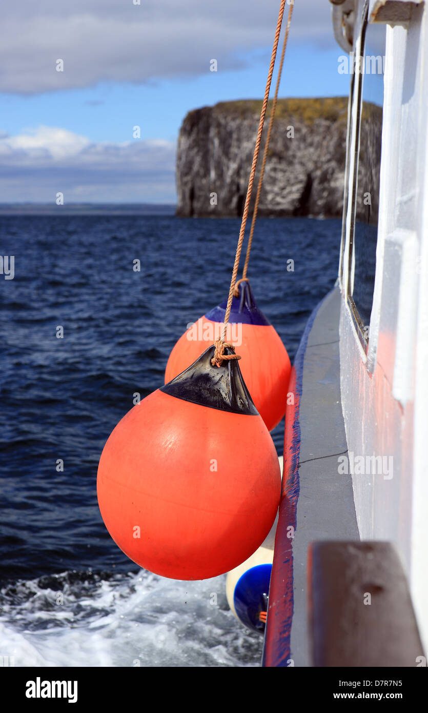 Orange Kotflügel an der Seite eines Bootes während auf hoher See mit der Felswand der Isle of May im Hintergrund Stockfoto
