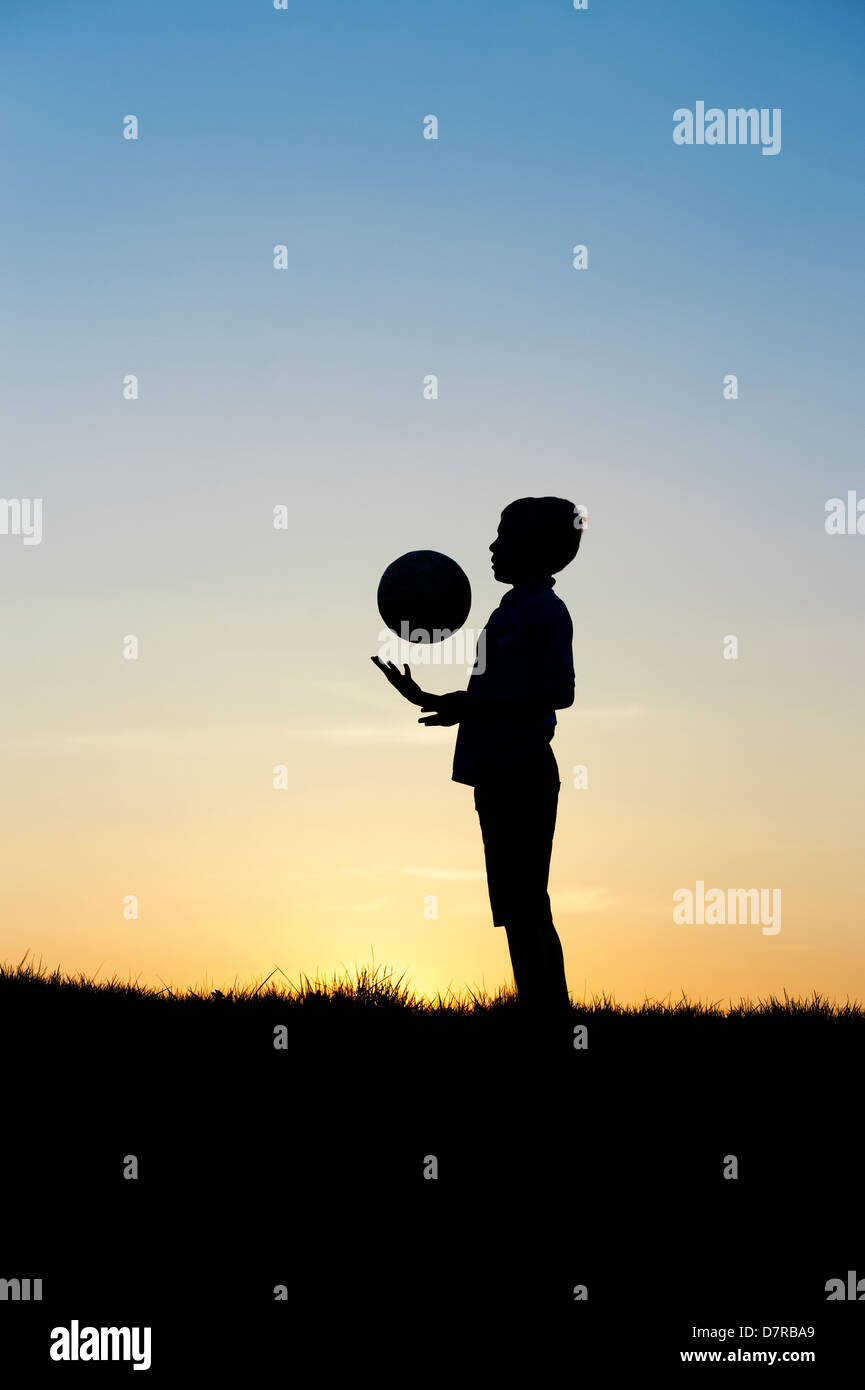 Jungen spielen mit einem Fußball bei Sonnenuntergang. Silhouette Stockfoto