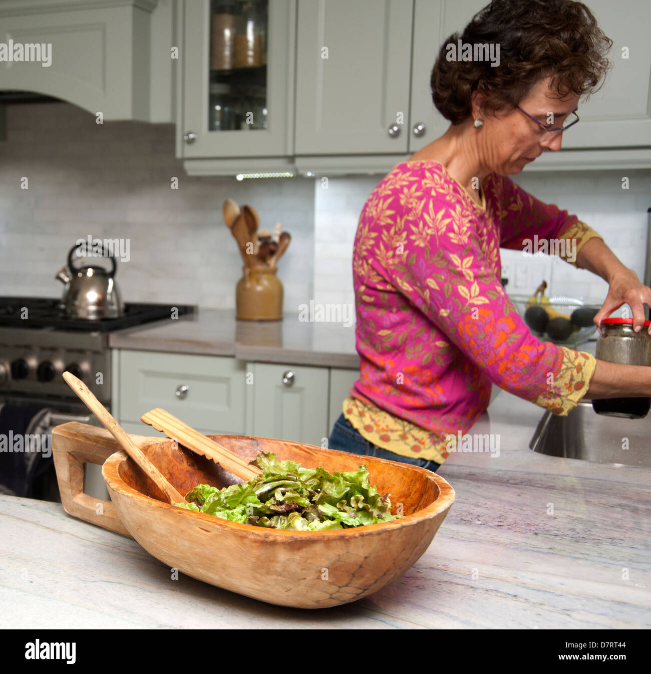 Frau in der Küche zu Hause Vorbereitung Abendessen mit einer Schüssel Salat im Vordergrund Stockfoto