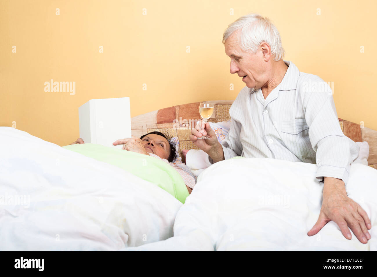 Älteres Paar im Bett ruhen mit Glas Alkohol und Buch Stockfoto