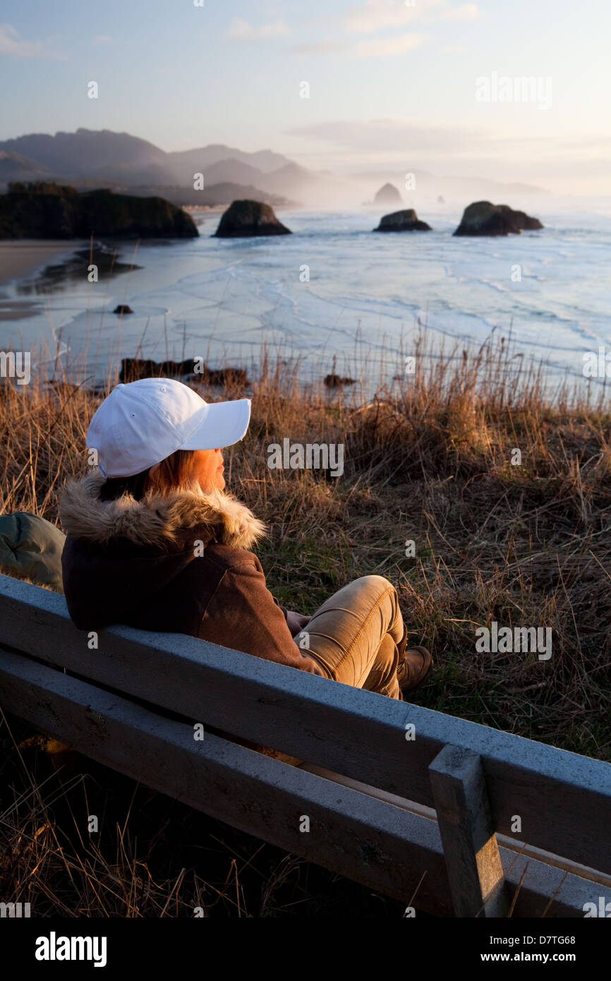 Frau sitzt auf einer Bank, die den Blick auf die Küste von Oregon mit Cannon Beach im Hintergrund Stockfoto