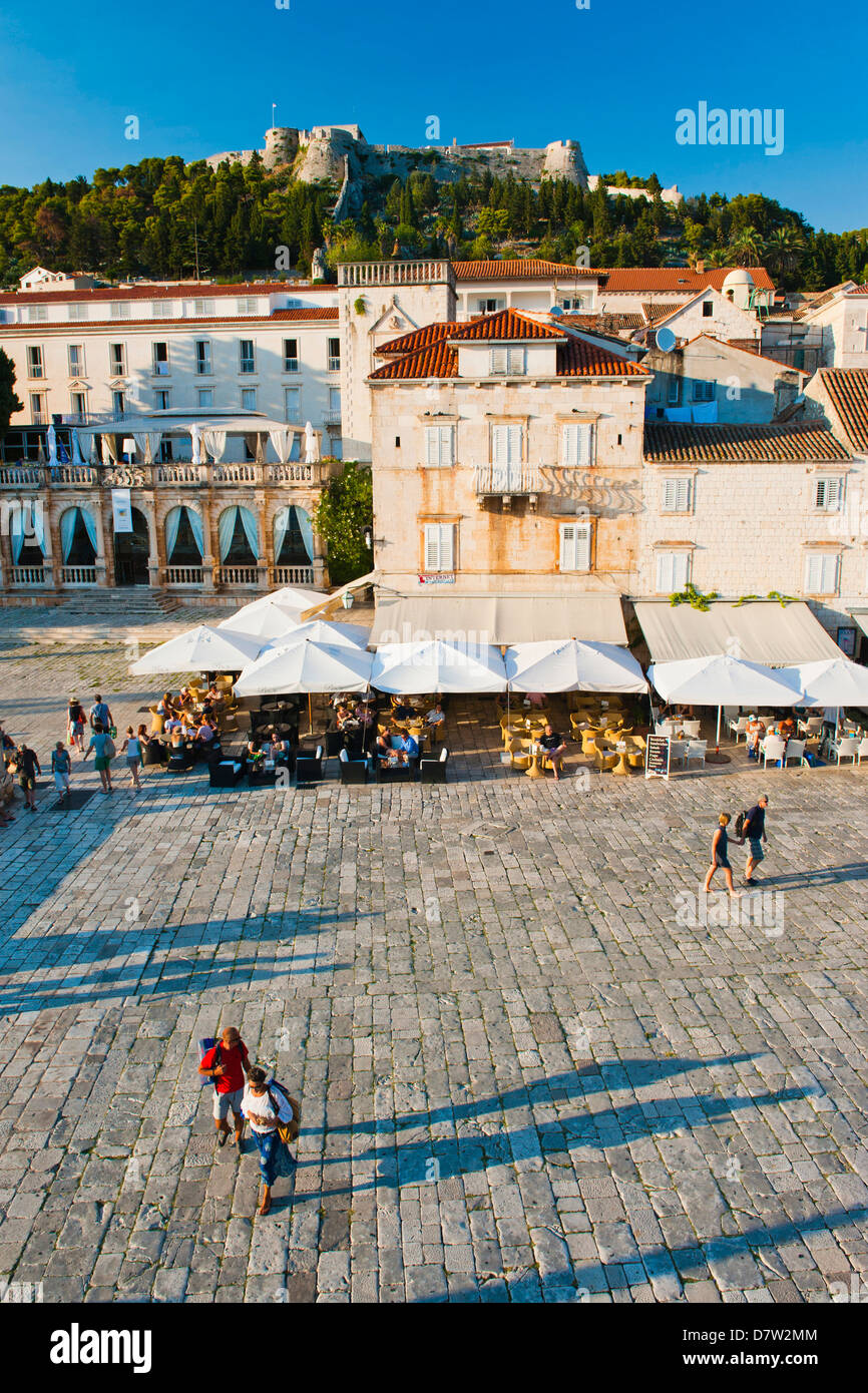 Touristen in St. Stephens Platz, mit der spanischen Festung (Fortica) oberhalb der Stadt Hvar, Insel Hvar, Dalmatien, Kroatien Stockfoto