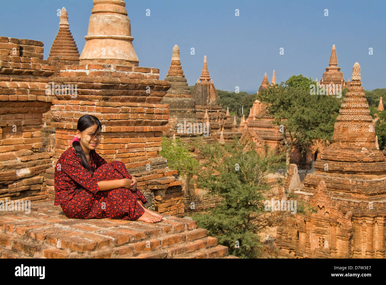 Junge burmesische Frau in einem roten Kleid sitzt auf dem Dach eines Tempels, Bagan (Pagan), Birma Stockfoto