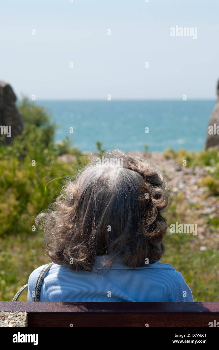 Eine Frau senior sitzen, Blick auf das Meer. Von hinten betrachtet. Stockfoto