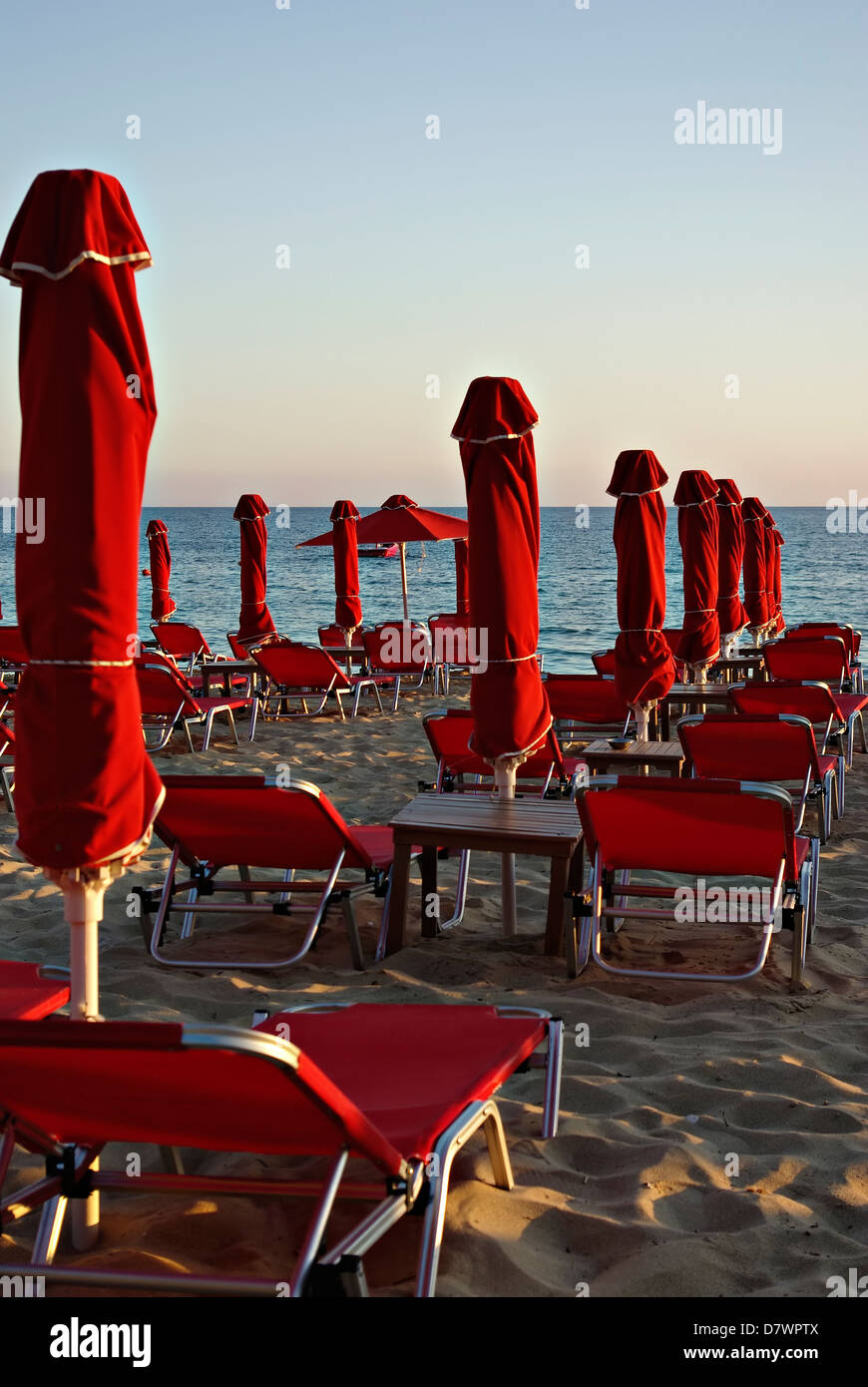 Rote Sonnenschirme und Sonnenliegen am Sandstrand bei Sommer Sonnenuntergang mit blauem Meer und Himmel im Hintergrund. Stockfoto