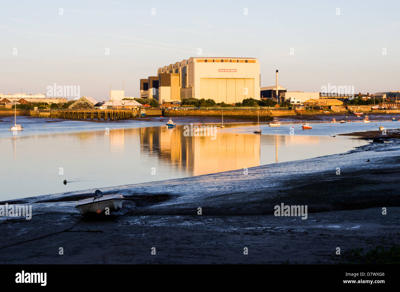 Ebbe, Boote auf den Boden, große Fabrik mit Spiegelbild im Kanal. In der Nähe von Barrow-in-Furness. Stockfoto