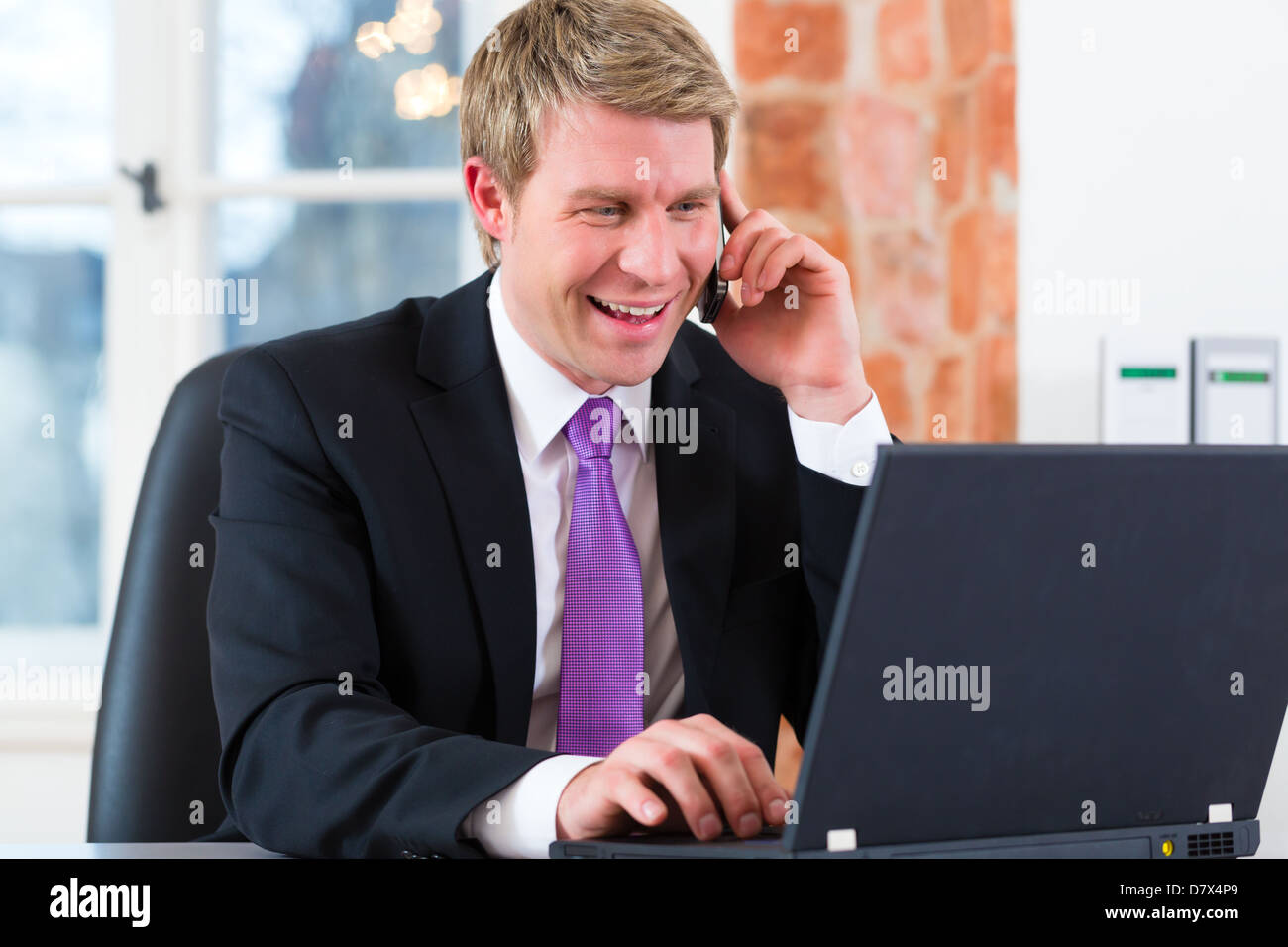 Junger Anwalt arbeitet in seinem Büro, er sitzt auf dem Schreibtisch und am Telefon ist ein Kunde oder Klient Stockfoto
