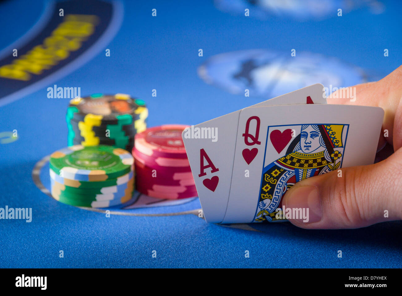 Black jack Spieler seine Karten prüfen, eine Hand mit dem Herz Ass und die Königin der Herzen auf einem blauen Poker Tisch in der Nähe Stapel Chips Stockfoto