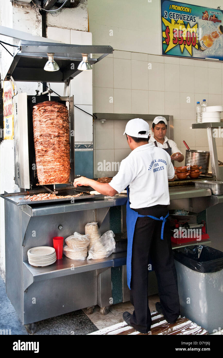 2 junge mexikanische Männer Arbeiter an Edelstahl Theke im Fastfood-Restaurant machen Tacos al Pastor aus Fleisch am Spieß braten Stockfoto