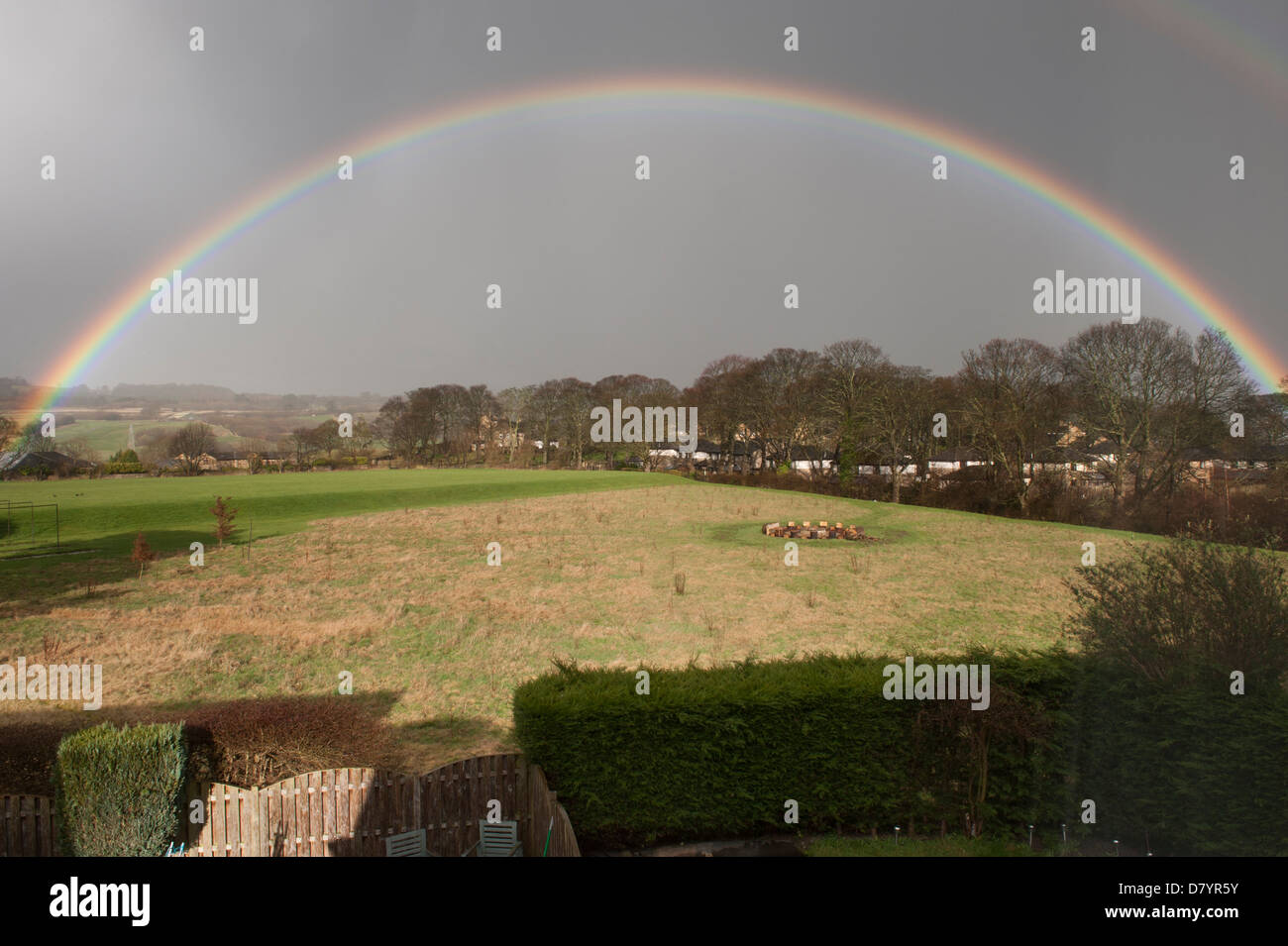 Wunderschöner Regenbogen, der einen perfekten Bogen über Regenwolken am Himmel über sonnenbeschienenen Feldern in ländlicher Landschaft bildet - Baildon, West Yorkshire, England, Großbritannien. Stockfoto