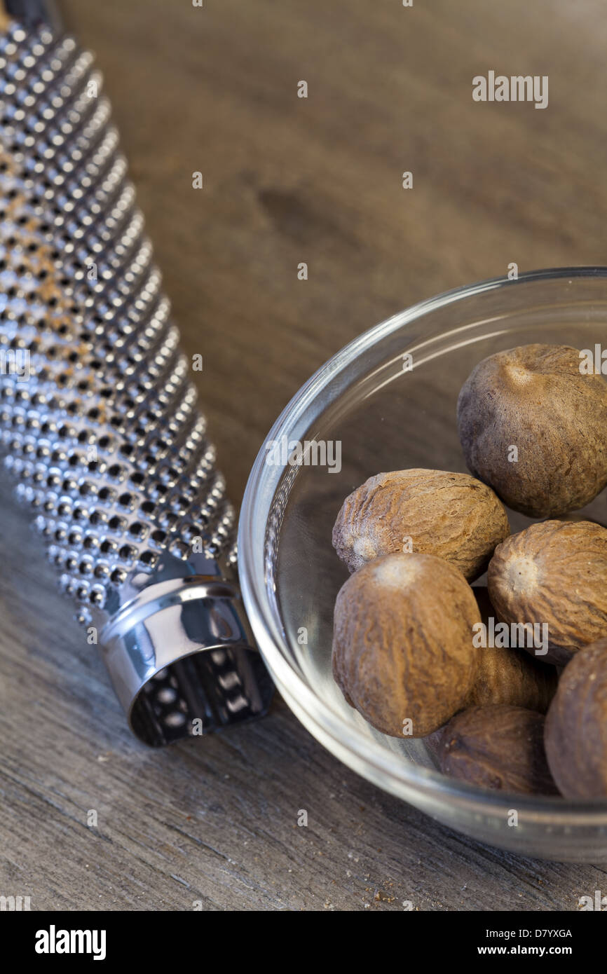 Einige ganze Muskatnuss in eine Glasschüssel neben einer Muskatnuss-Reibe Stockfoto