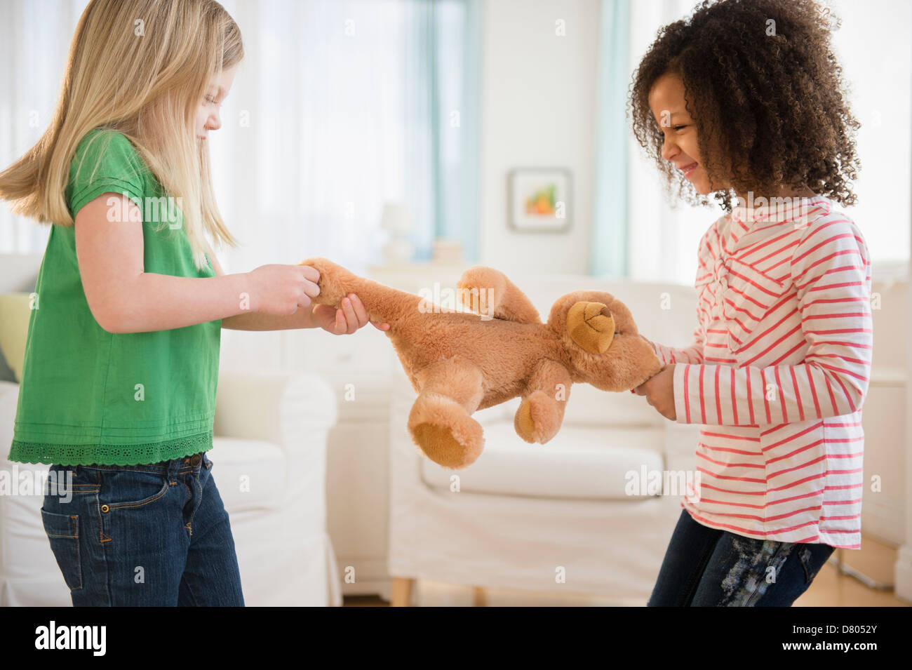 Mädchen kämpfen über Teddybär im Wohnzimmer Stockfoto