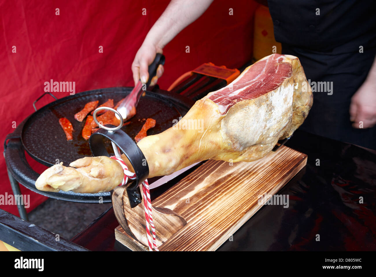 Serrano-Schinken auf ein Stativ und Mann Kochen Chorizo Wurst in ein outdoor-event Stockfoto
