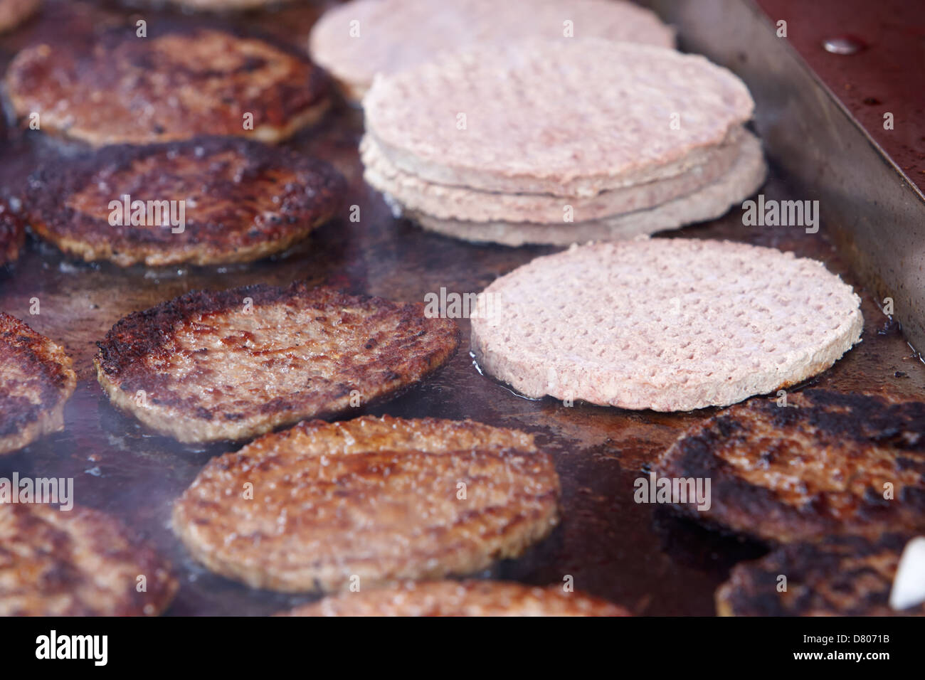 Roh und gekocht verarbeitet Hamburger auf einem kommerziellen flachen Grill auf ein outdoor-event Stockfoto