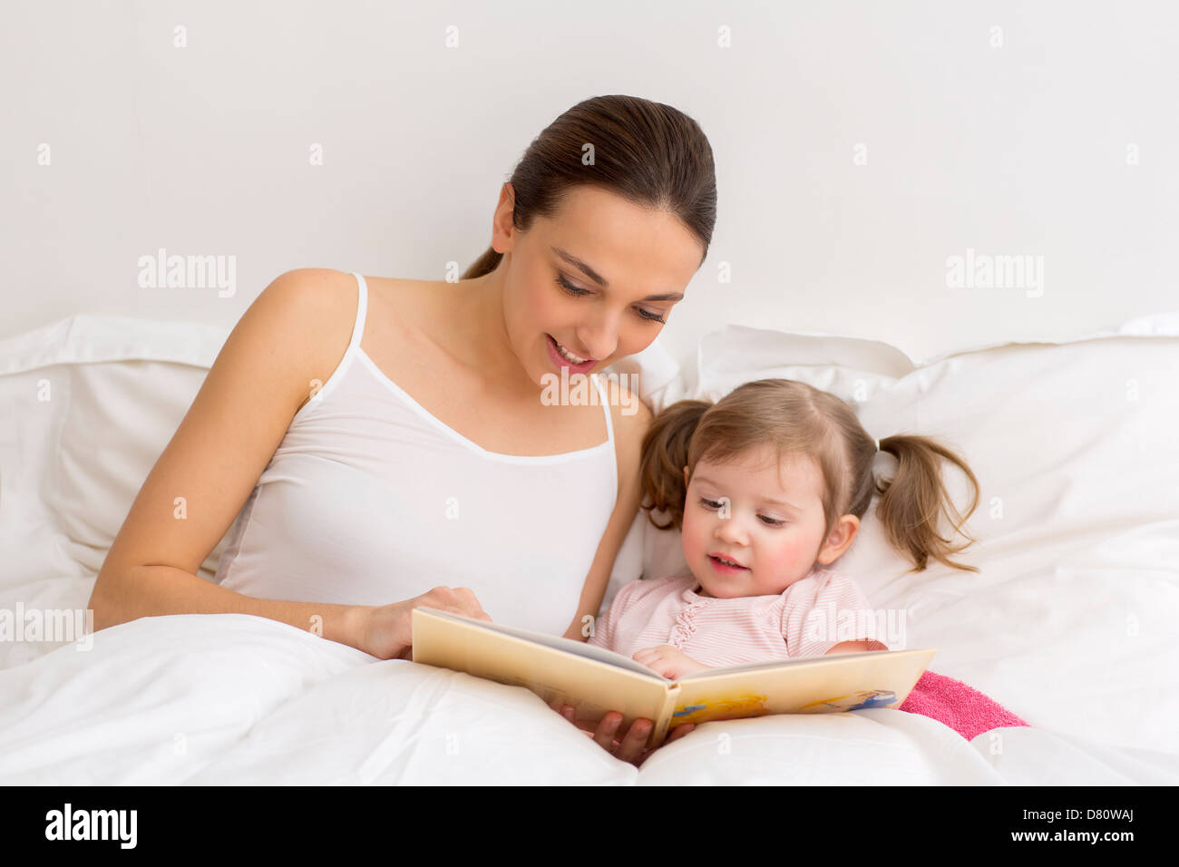 Kleines Mädchen, ein Buch zu lesen, mit ihrer Mutter in weiße Schlafzimmer Stockfoto