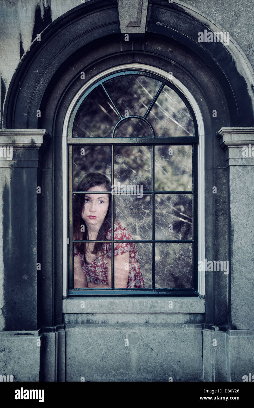 traurig aussehende Frau hinter einem alten Fenster Stockfoto