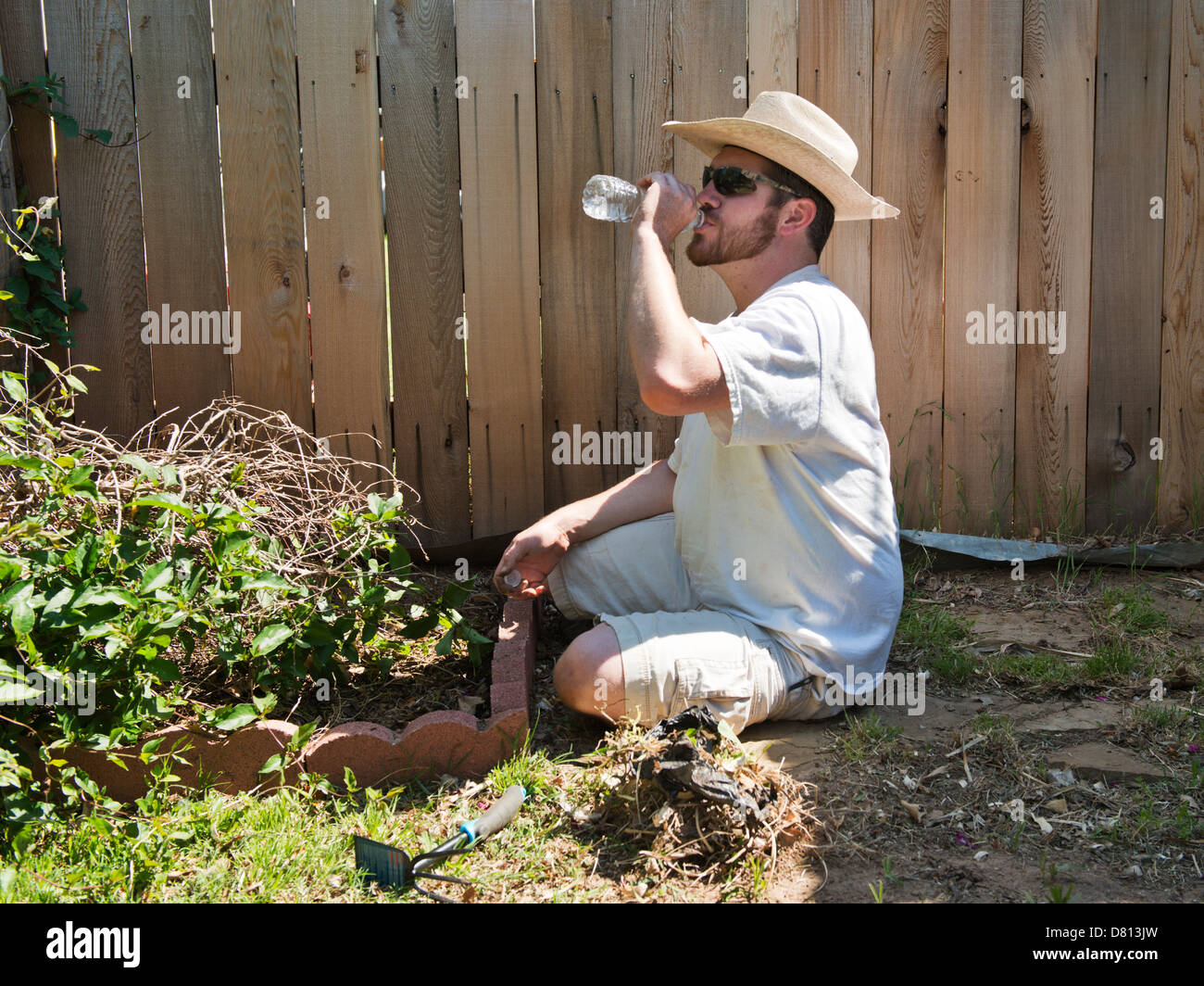 Ein kaukasischer Mann, 27 Jahre alt, Getränke Mineralwasser bei der Gartenarbeit an einem warmen Frühlingstag. Oklahoma, USA. Stockfoto