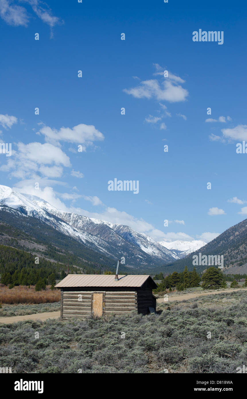 Eine alte verlassene Blockhütte befindet sich mit einem atemberaubenden Blick auf den schneebedeckten Rocky Mountains von Colorado. Stockfoto