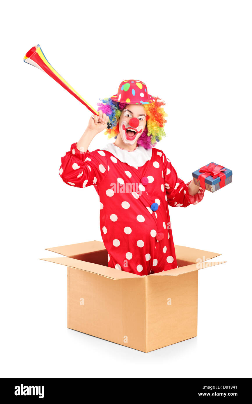 Verspielter Clown kommt aus einer Box und halten Sie ein Horn und ein Geschenk, isoliert auf weißem Hintergrund Stockfoto