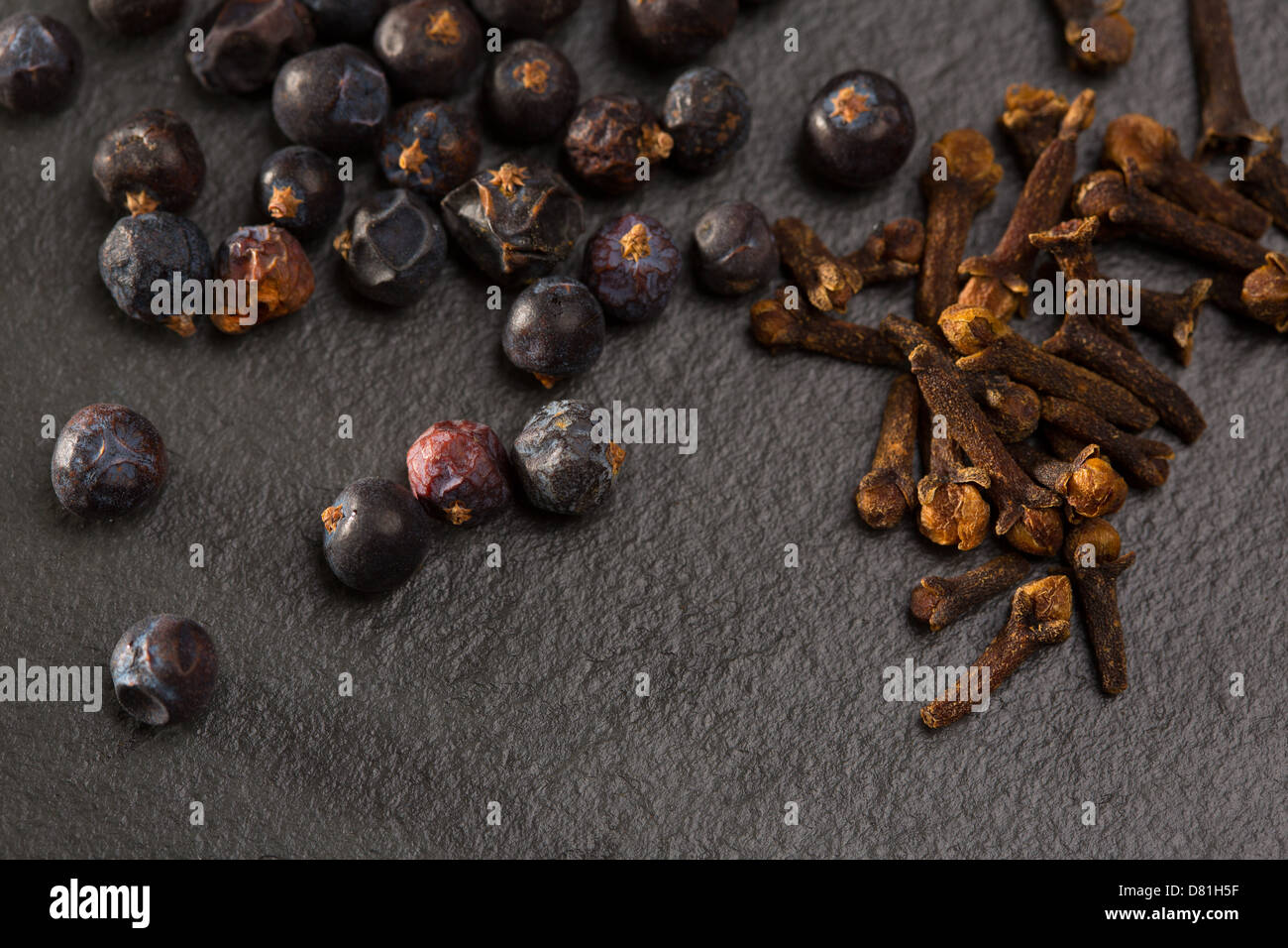 Nelken und Wacholder Beeren Gewürze auf schwarzem Schiefer Stein Hintergrund Stockfoto
