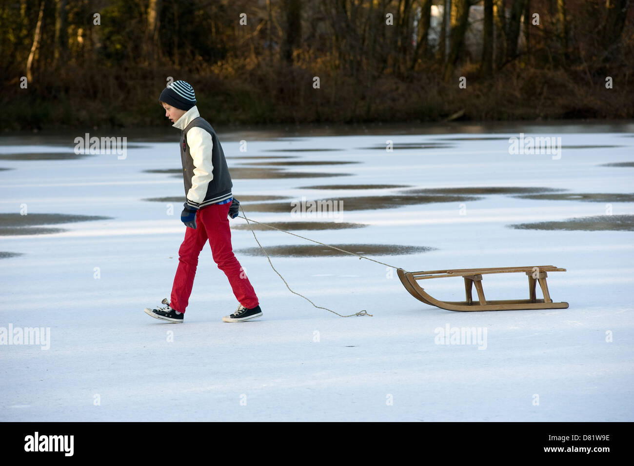 Ein Junge ist Fuß auf einem zugefrorenen Teich mit seinem Schlitten Stockfoto