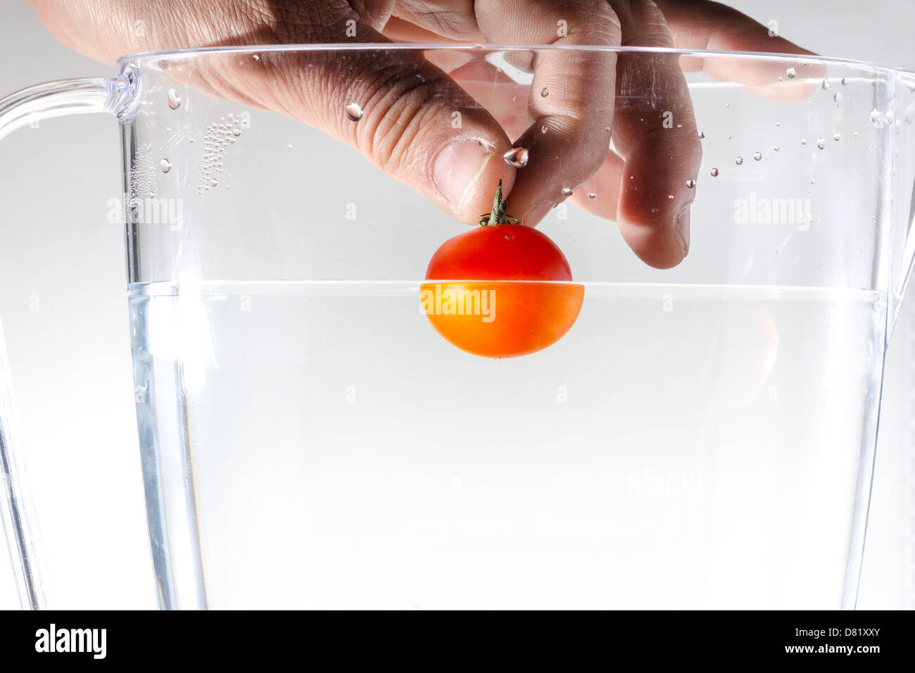 Hand, die eine Tomate ins Wasser zu werfen, ist Stockfoto