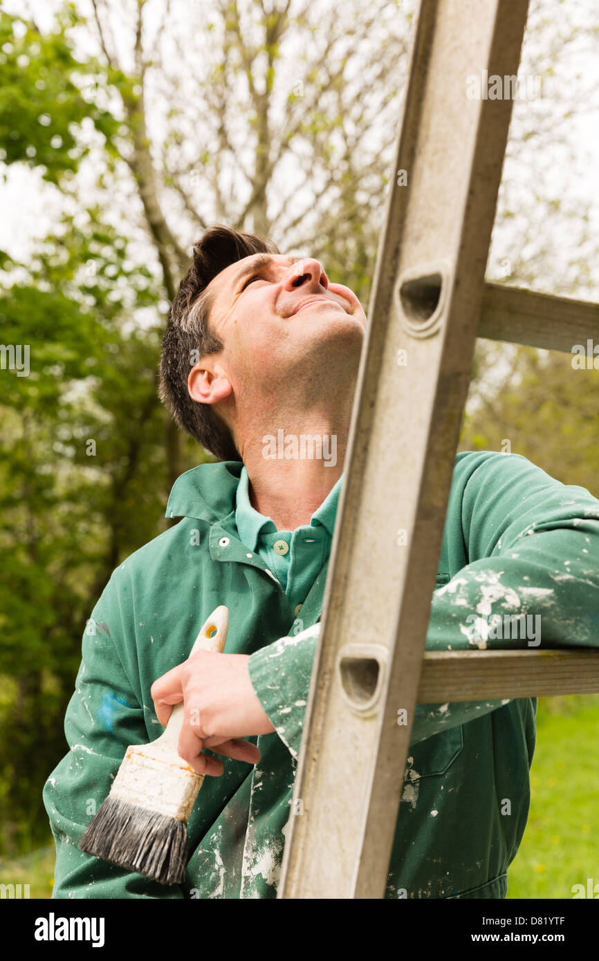 Mann trägt Overalls stützte sich auf eine Leiter und einen Pinsel halten Stockfoto