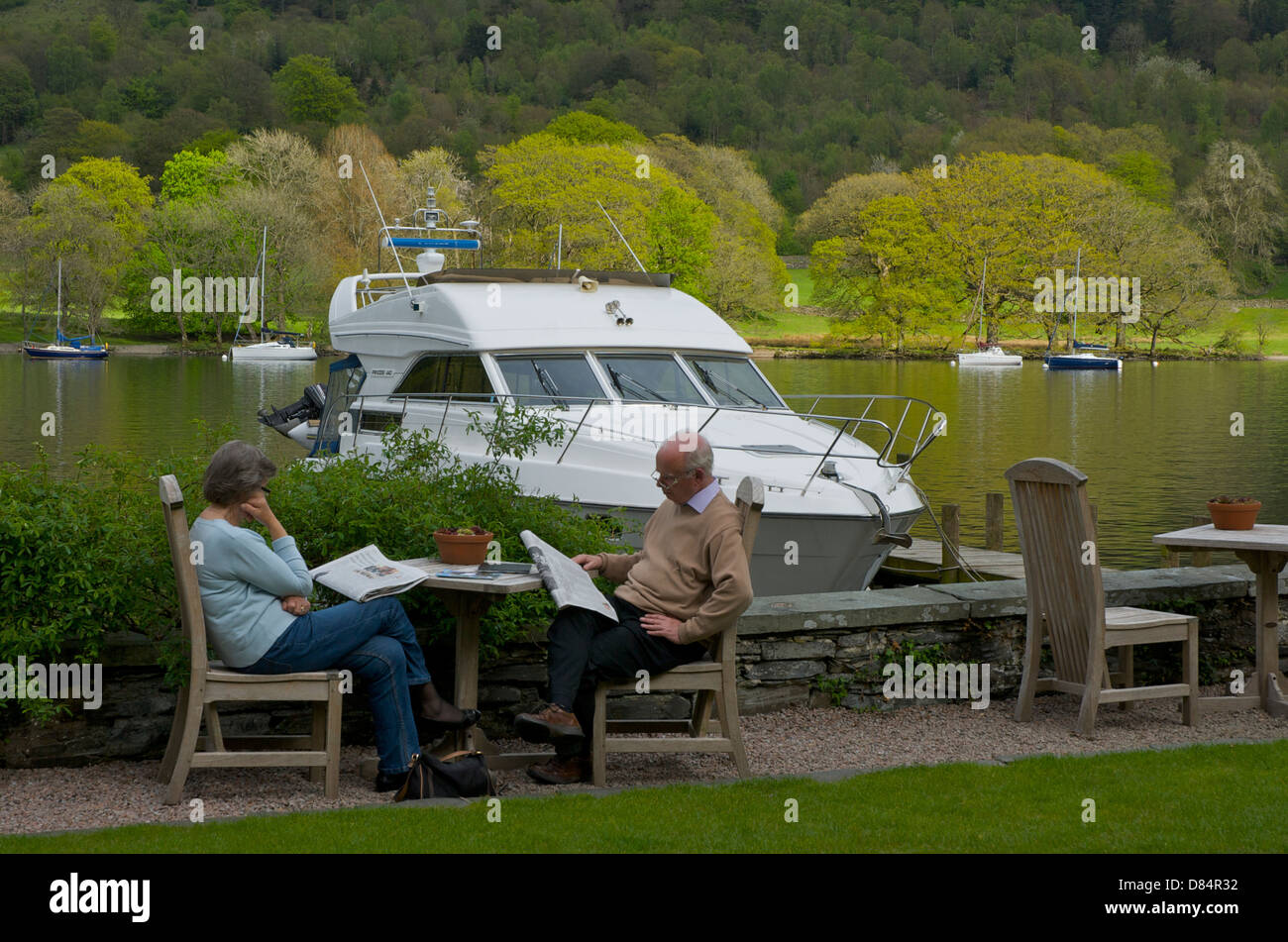 Paar mittleren Alters sitzen, lesen die Zeitungen im Garten des Seehotel, See, Lake District, Cumbria, England U Stockfoto