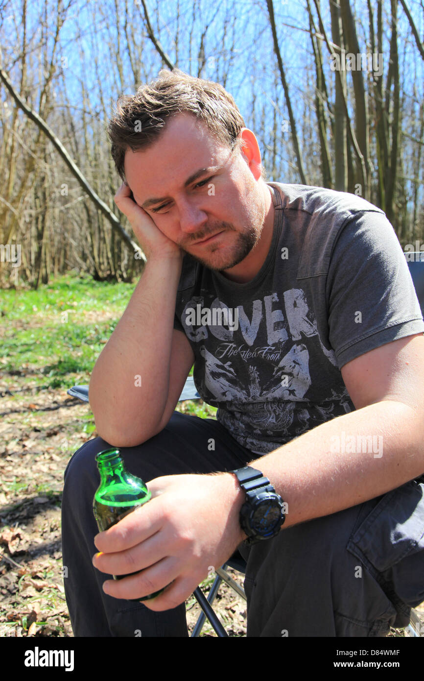 Mann in seinen frühen satt dreißiger Jahren Bier zu trinken und auf der Suche beim Zelten im Wald. Stockfoto