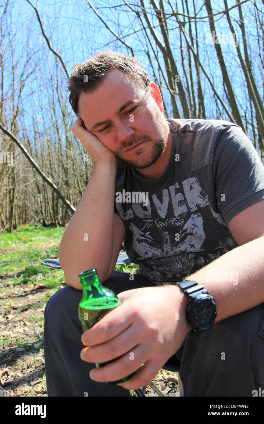 Mann in seinen frühen satt dreißiger Jahren Bier zu trinken und auf der Suche beim Zelten im Wald. Stockfoto