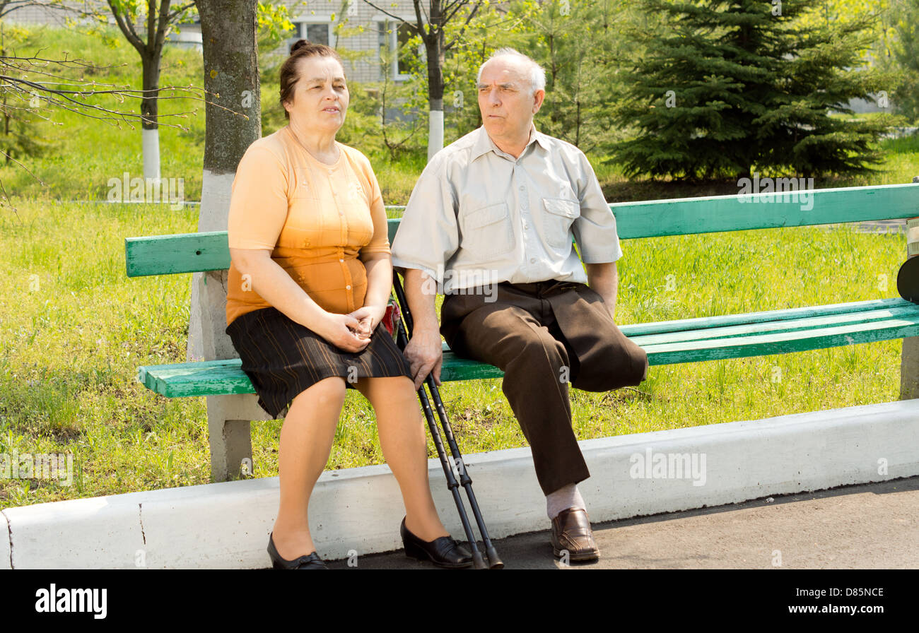 Mann mit gebrochenen Fuß sitzt auf der Parkbank mit seiner Frau Stockfoto