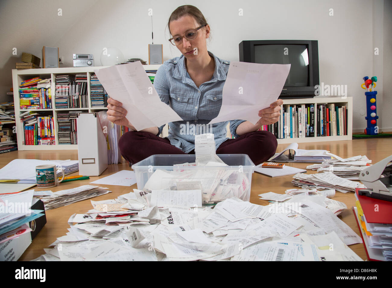 Junge Frau sitzt zu Hause und Rechnungen, Quittungen und andere Papiere für ihre Steuererklärung zu klären. Stockfoto