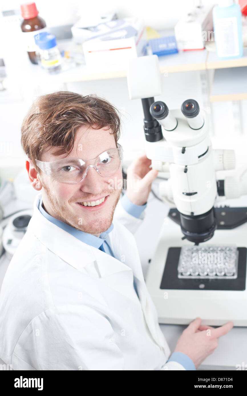 Deutschland, Porträt eines jungen Wissenschaftlers mit Mikroskop im Labor, Lächeln Stockfoto