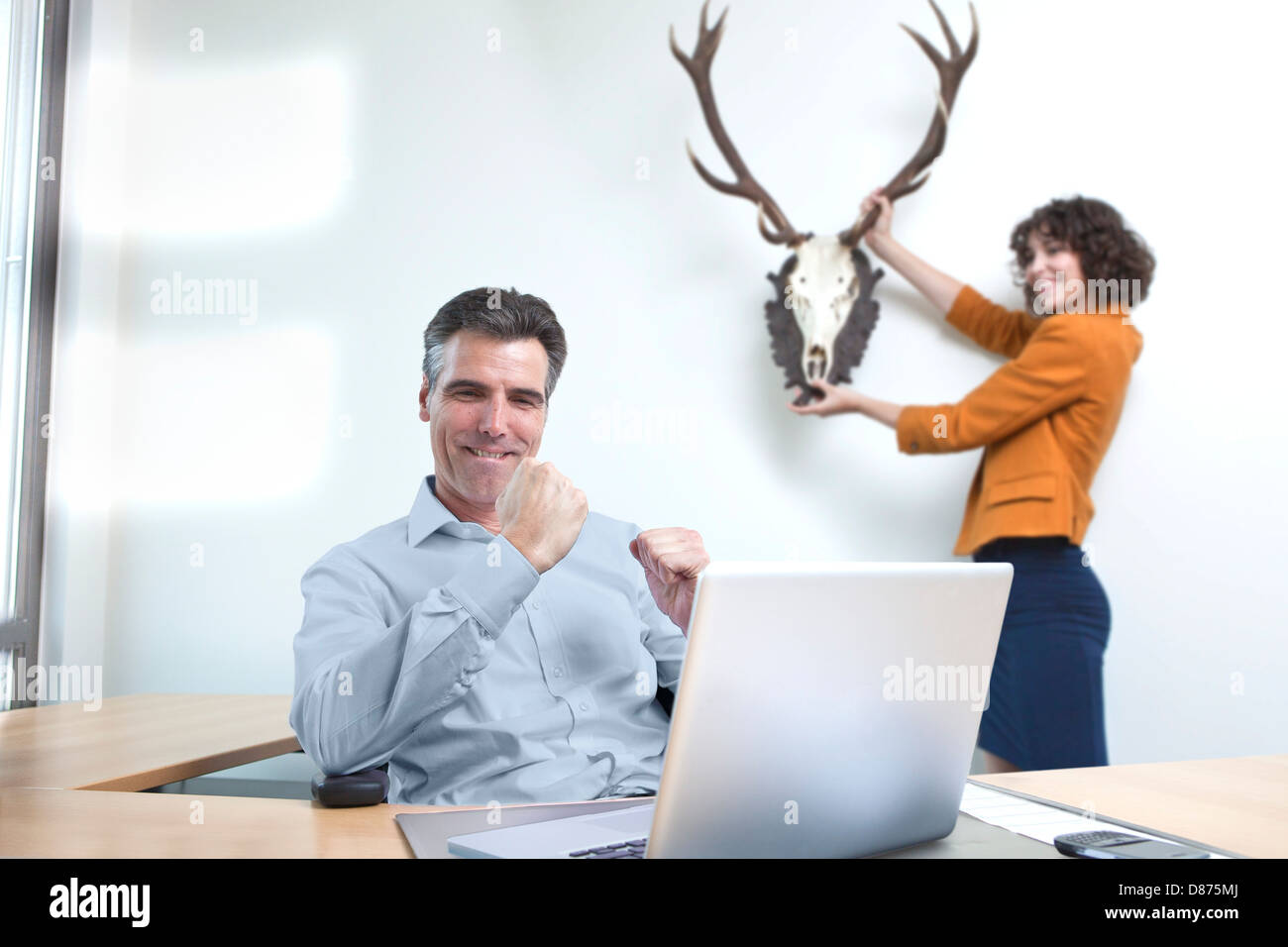 Blick auf Laptop, während der Assistent aufhängen Trophäe für ihn lächelnd Geschäftsmann Stockfoto