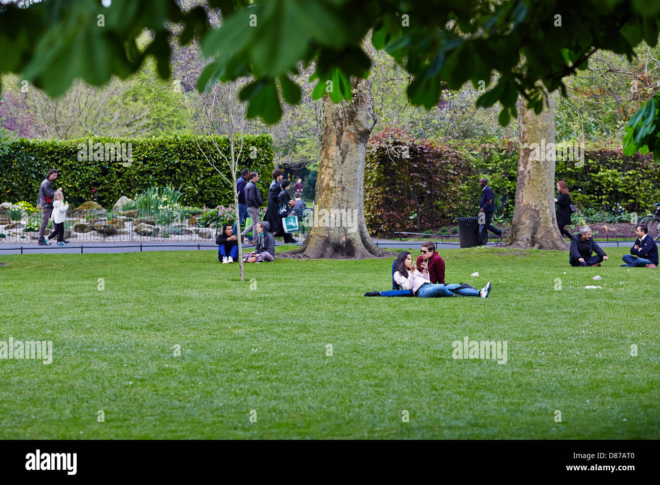 Junge Leute sitzen und entspannen Sie an einem sonnigen Tag in St. Stephens Green Park, Dublin, Republik Irland Stockfoto