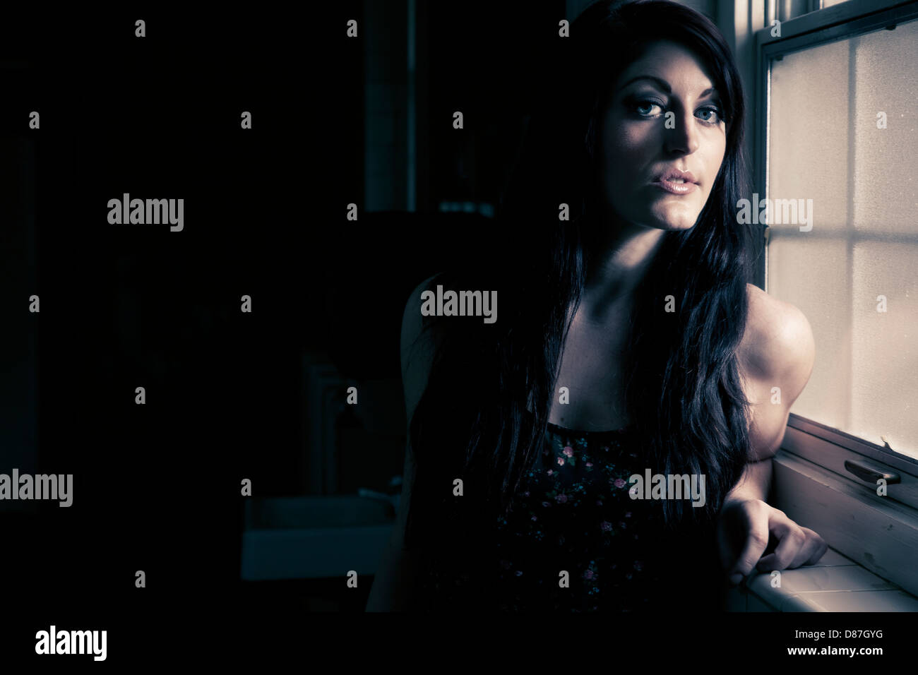 Frau im dunklen Raum neben beleuchteten Fenster Stockfoto