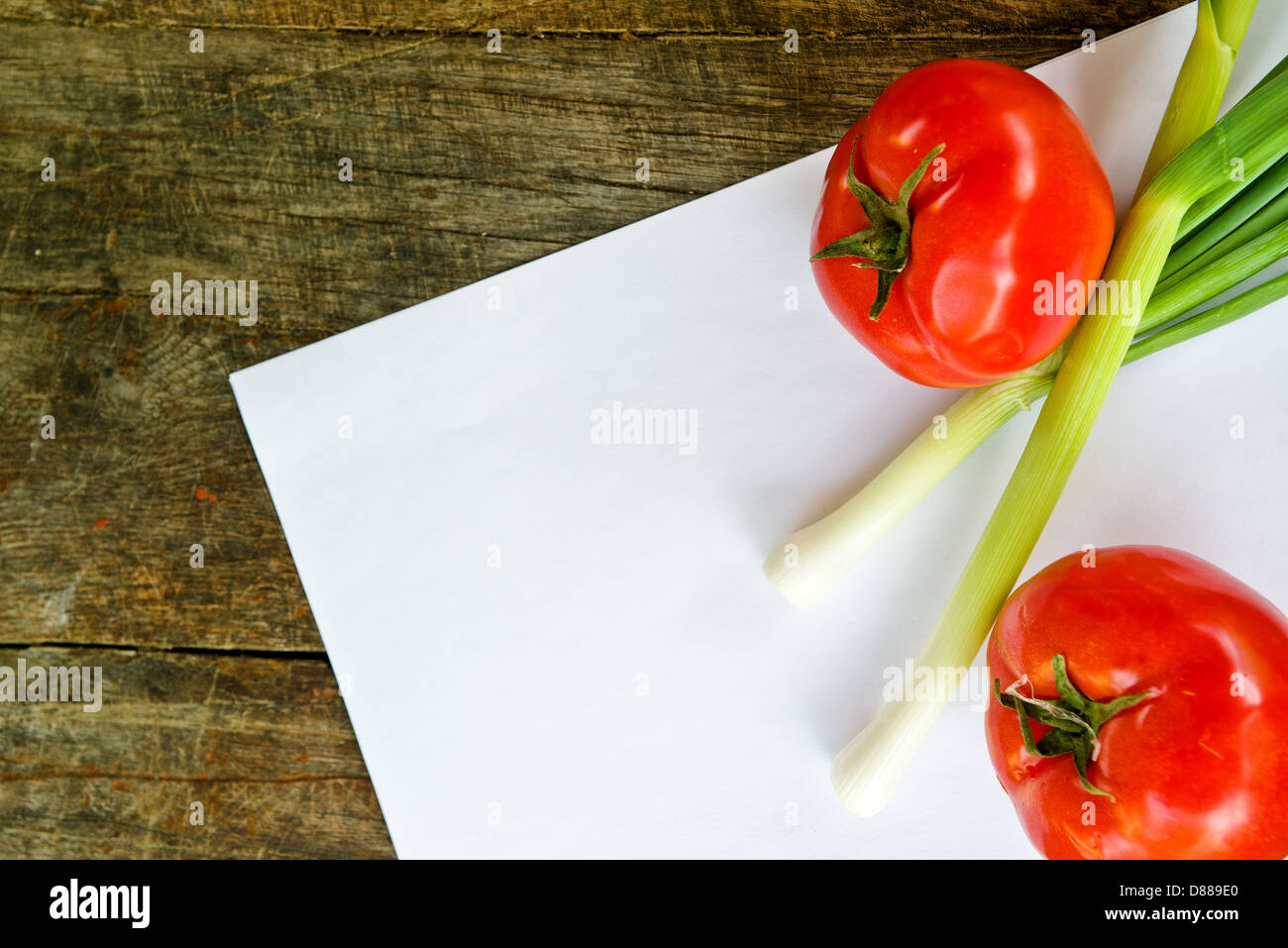 Tomaten und Frühlingszwiebeln auf Papier für Rezept Notizen auf Holztisch. Stockfoto