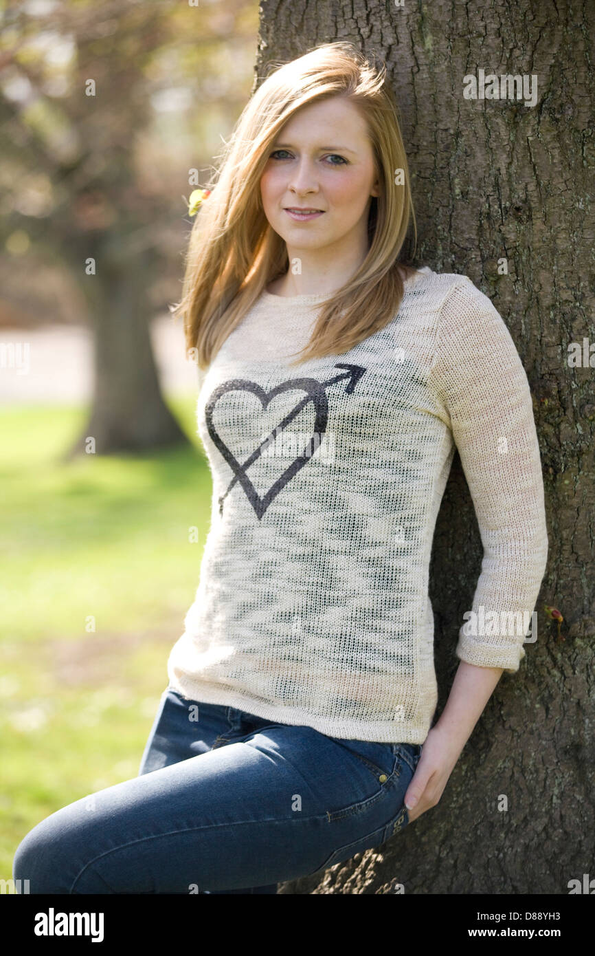 Hübsche blonde Frau an einen Baum gelehnt. Stockfoto