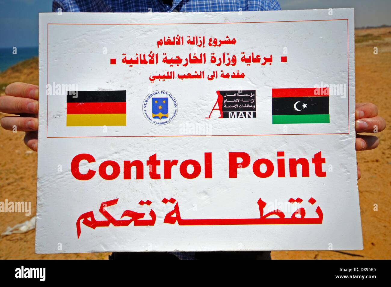 Ein Schild mit der englischen und arabischen Schrift "Kontrollposten" ist der Einstiegspunkt für eine Explosion Boden in der Nähe von Tripolis, Libyen, 6. Mai 2013 abgebildet. Das Obermaterial in Arabisch schreiben gibt Informationen über das Projekt von der deutschen St. Barbara-Stiftung und deren Finanzierung durch das deutsche Auswärtige Amt. Seit seiner Gründung im Jahr 1995, der St. Barbara Foundation unterstützt die Clearance von Waffen und Sprengkörper der ehemaligen Konfliktgebieten und Krieg-Theater und leistet humanitäre Hilfe. Die NGO ist seit Anfang 2012 in Libyen aktiv und finanziert, unter anderem mit Hilfe der deutschen Bundesrepublik Fo Stockfoto