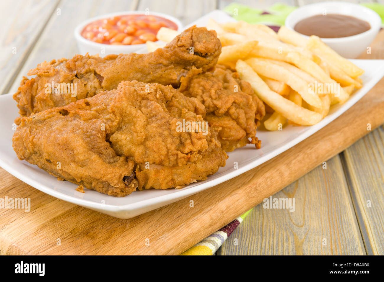 Fried Chicken & Chips - Hähnchenteile auf den Knochen in würziger Mehl überzogen und frittiert. Pommes frites, Bohnen und Soße Seiten. Stockfoto