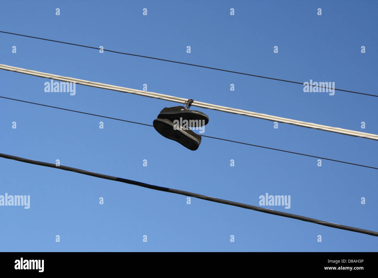 Ein Paar Schuhe hängt an Stromleitungen, ein häufiges urbanes Phänomen. Die Schuhe werden an den Schnürsenkeln aufgehängt und bilden einen auffälligen visuellen Kontrast zum Himmel und der Umgebung. Stockfoto
