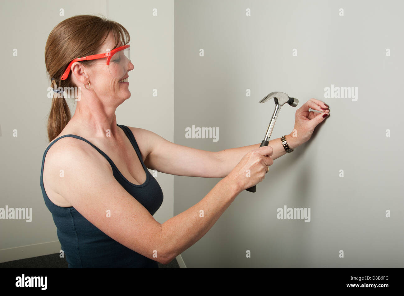 Frau mit einem Hammer auf einen Nagel in die Wand schlagen Stockfoto