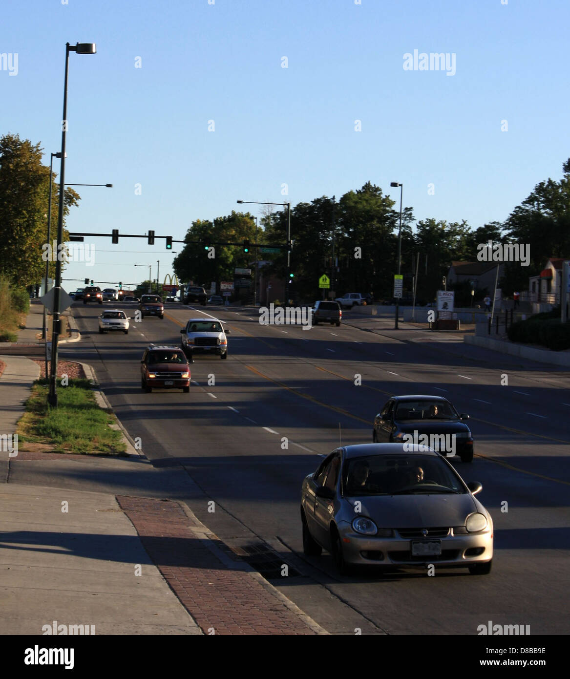 Eine Straßenszene mit Autos, die auf einer befahrenen Straße fahren. Das Bild erfasst die Bewegungen von Fahrzeugen auf der Straße und zeigt das städtische Leben und den Verkehrsfluss. Gebäude, Bäume und andere urbane Elemente sind im Hintergrund sichtbar und weisen auf eine Stadt oder Vorstadt hin. Stockfoto