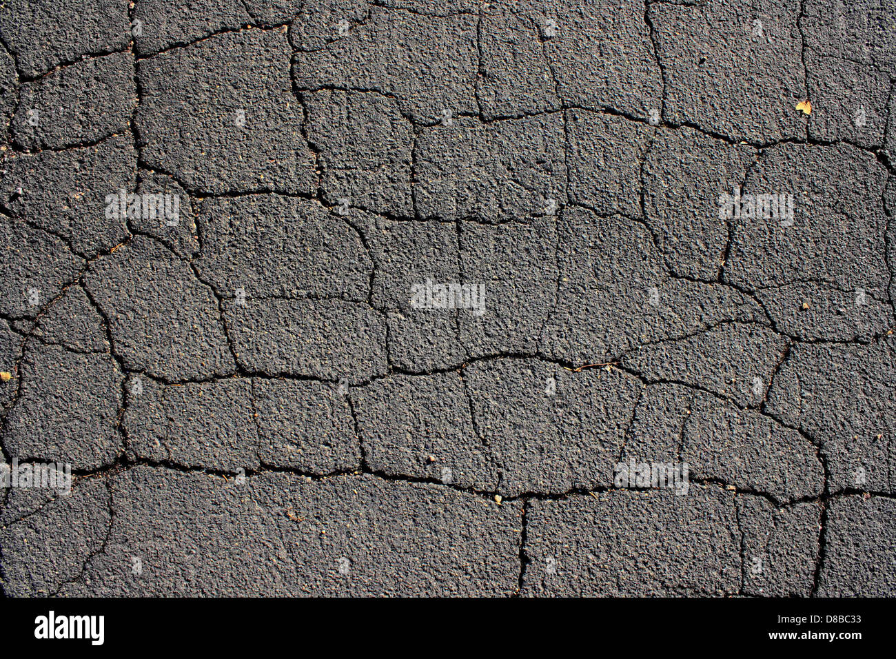 Eine Nahaufnahme von gerissenem Asphaltbelag mit schwarzer Oberfläche. Die Struktur hebt Schäden durch Verschleiß hervor, die wahrscheinlich durch Witterung oder starken Verkehr verursacht werden. Stockfoto