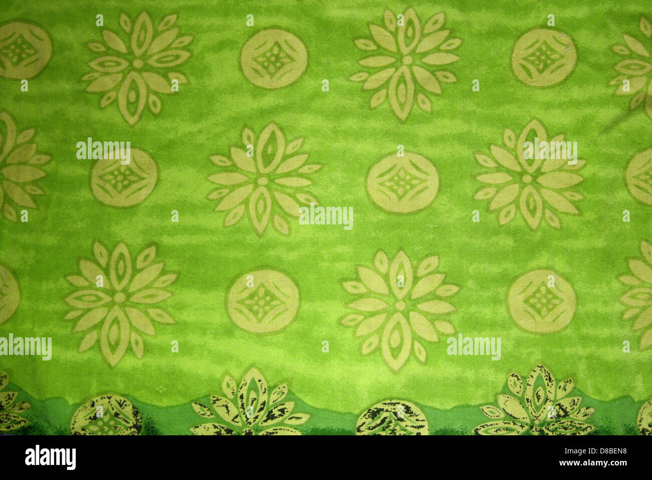 Eine Nahaufnahme aus grünem Stoff mit gelben Blumen und kreisförmigen Mustern. Dieses Textildesign zeigt ein lebendiges und dekoratives Muster, das häufig in Kleidung oder Wohnkultur verwendet wird. Stockfoto