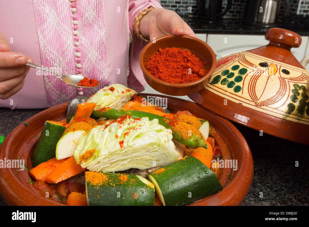 Traditionellen marokkanischen Einwanderer Frau in Europa hinzufügen von Gewürzen zu ihr Tajine während des Ramadan in ihrer modernen Küche Stockfoto