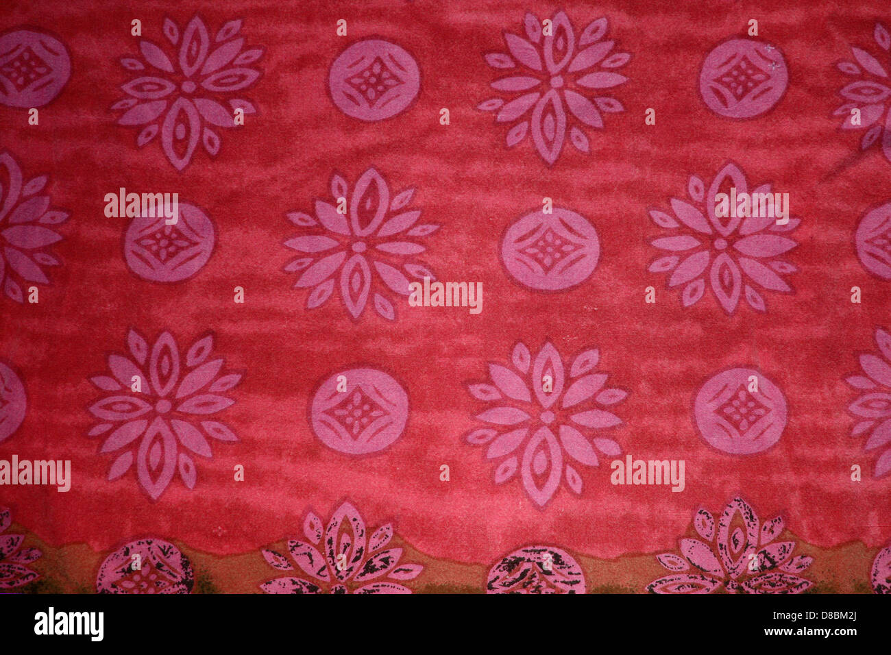 Ein Nahbild aus rotem Stoff mit einem Muster aus rosa Blumen und Kreisen. Die Textil-Textur ist auffällig und zeigt komplizierte Details in Design und Farbkombination. Stockfoto