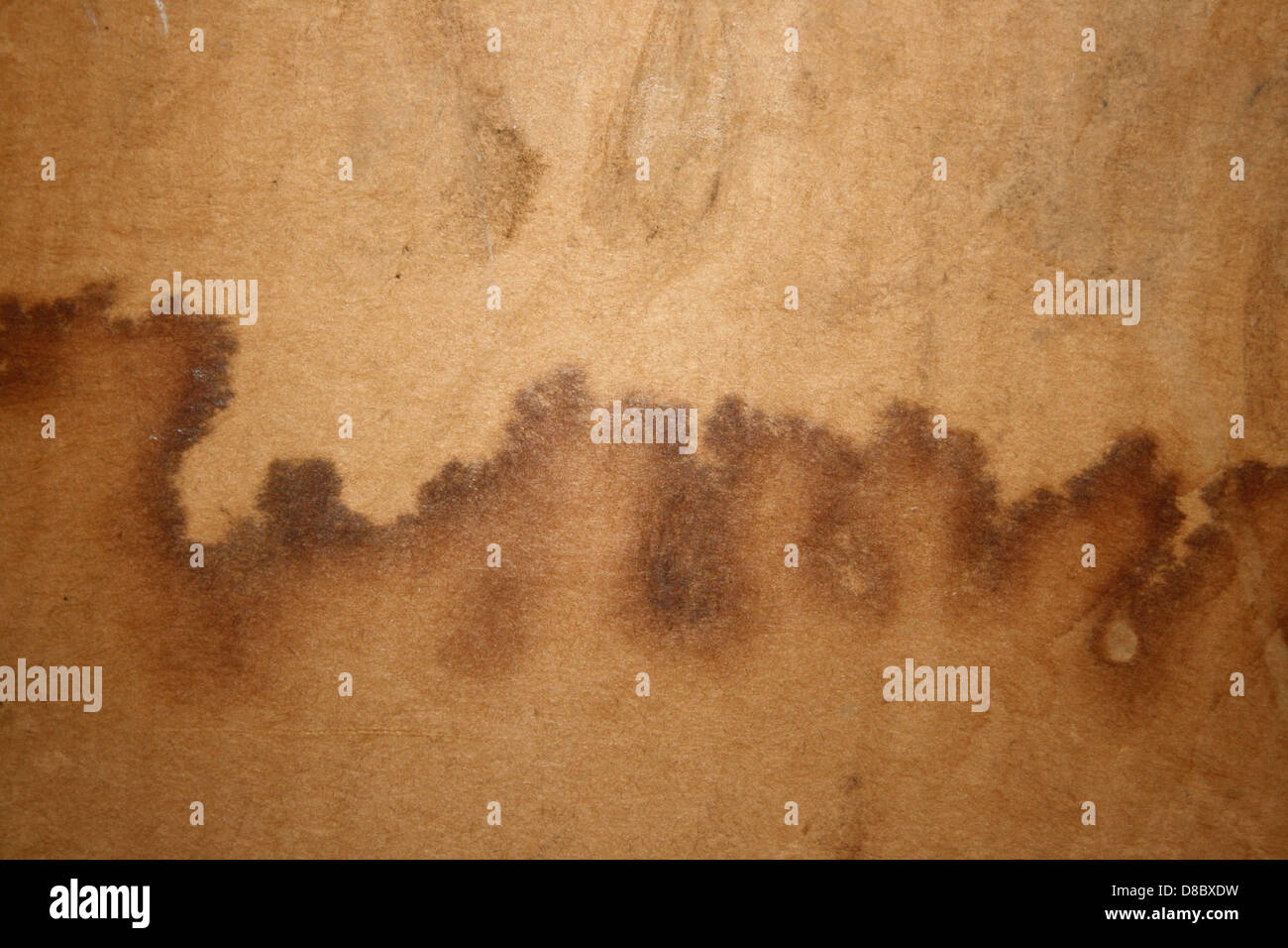 Diese Abbildung zeigt Wasserflecken auf der Oberfläche von Pappe und hebt das unregelmäßige Muster hervor, das durch Feuchtigkeit verursacht wird. Die Flecken erzeugen ein strukturiertes und verwittertes Aussehen. Stockfoto