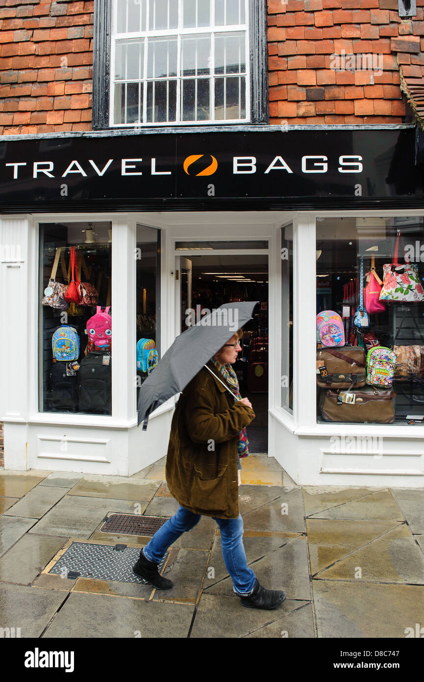 Shopper zu Fuß eine Reisetasche Shop im Regen mit Regenschirm in Salisbury, Wiltshire GROSSBRITANNIEN Stockfoto