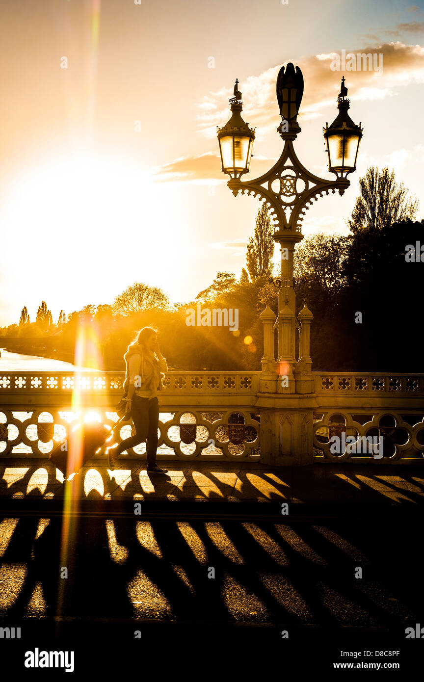 Beleuchtetes kaukasisches Touristenweibchen, das einen fahrbaren Koffer über die verzierte Lendal Bridge mit dem Fluss Ouse in der Ferne zieht. Stockfoto